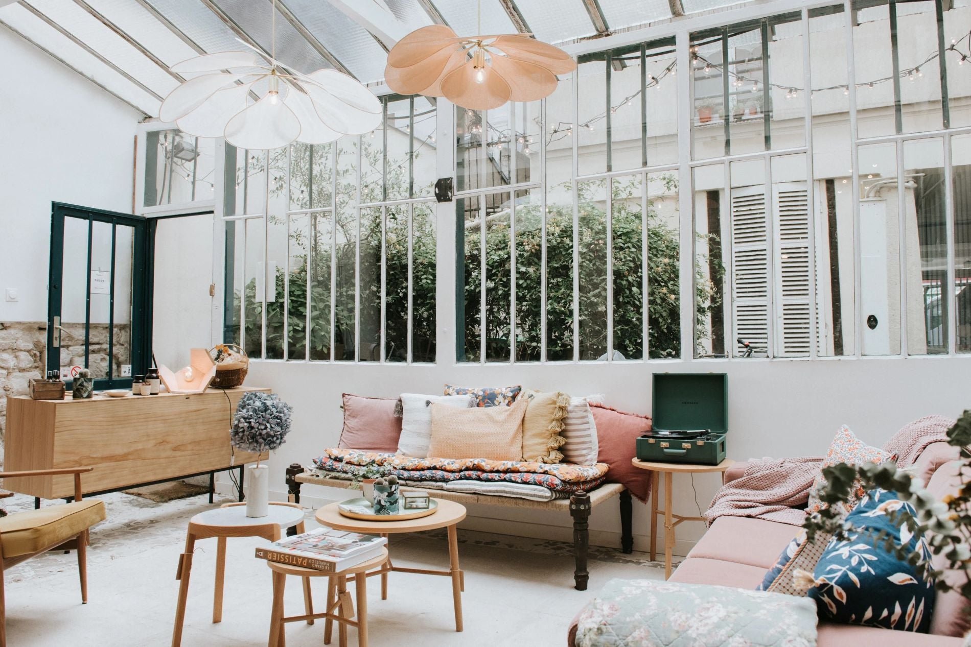 Photo montrant un salon avec un canapé sous une verrière, accompagné d'un lit indien recouvert de coussins. On peut également apercevoir des tables basses avec des fleurs.